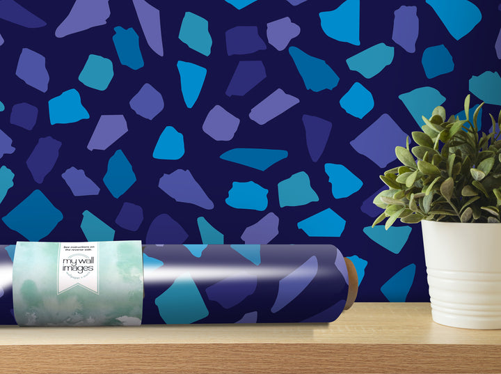 a roll of wallpaper with a blue and purple pattern, placed on a wooden shelf next to a potted plant.