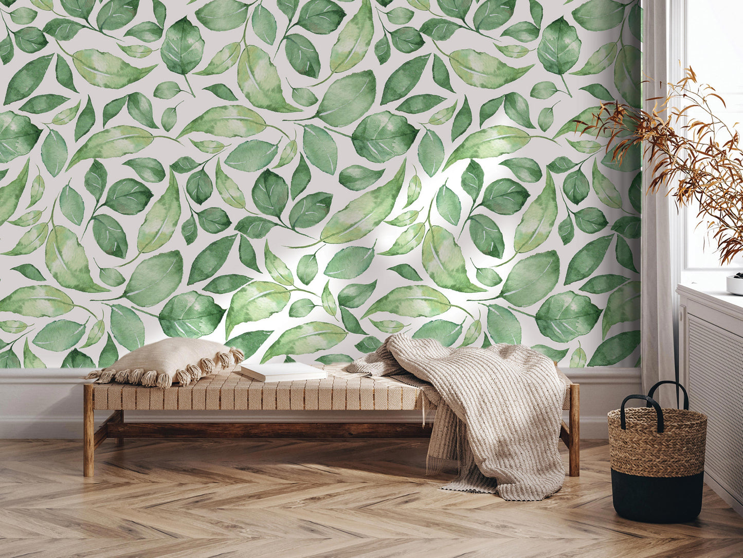 a living room with a large wallpapered wall adorned with a pattern of green leaves. In the foreground, there is a wooden bench with a blanket draped over it, and a woven basket next to it. The room has a chevron patterned floor, and a window can be seen on the right side of the image.
