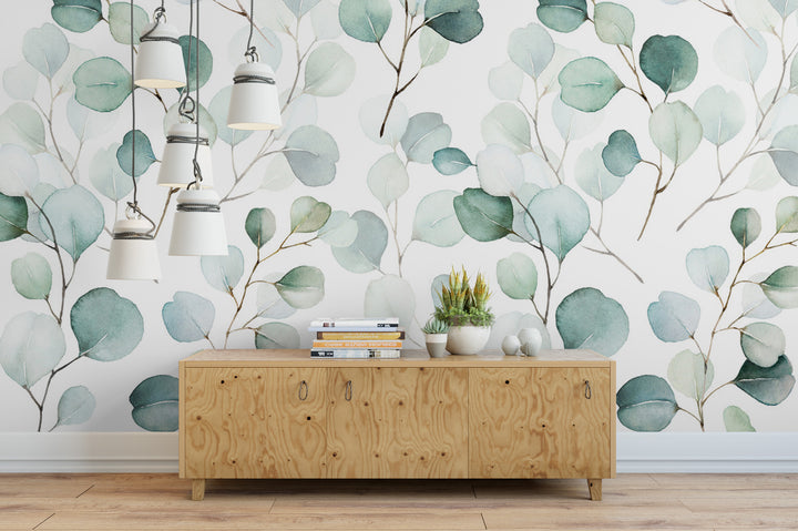 a wooden cabinet with a stack of books on top, set against a wall with a watercolor-style wallpaper pattern of green leaves.