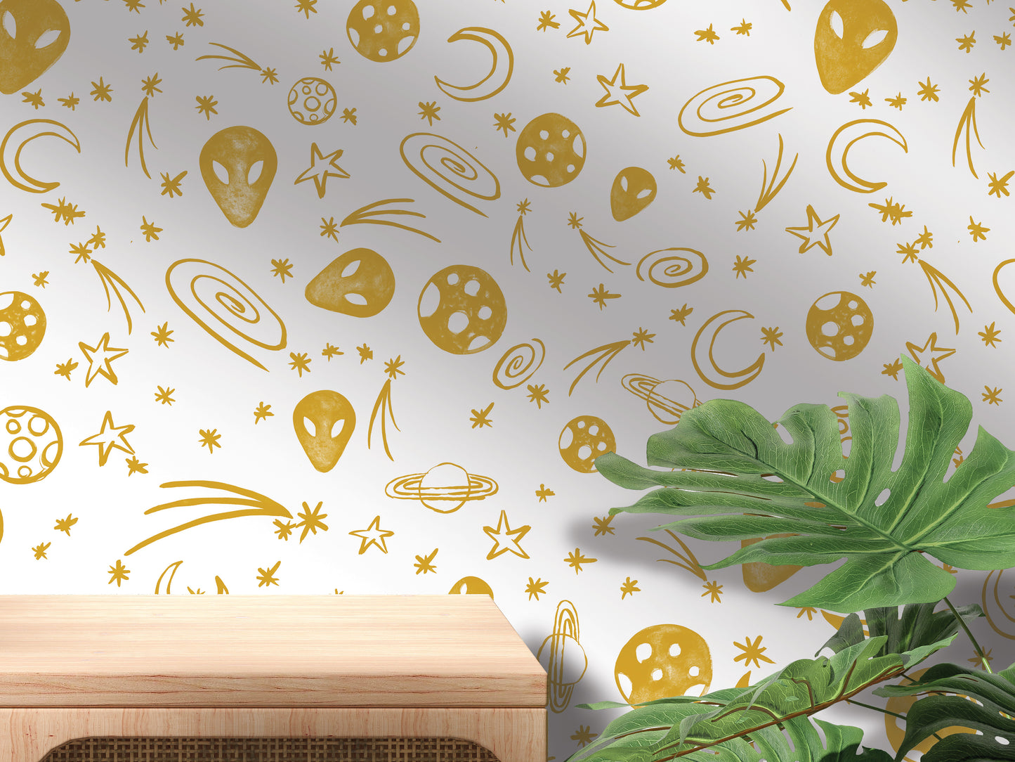 a wall with a pattern of gold stars, planets, and other celestial objects, creating a space-themed design. In the foreground, there is a wooden table and a plant, adding a touch of nature to the scene.