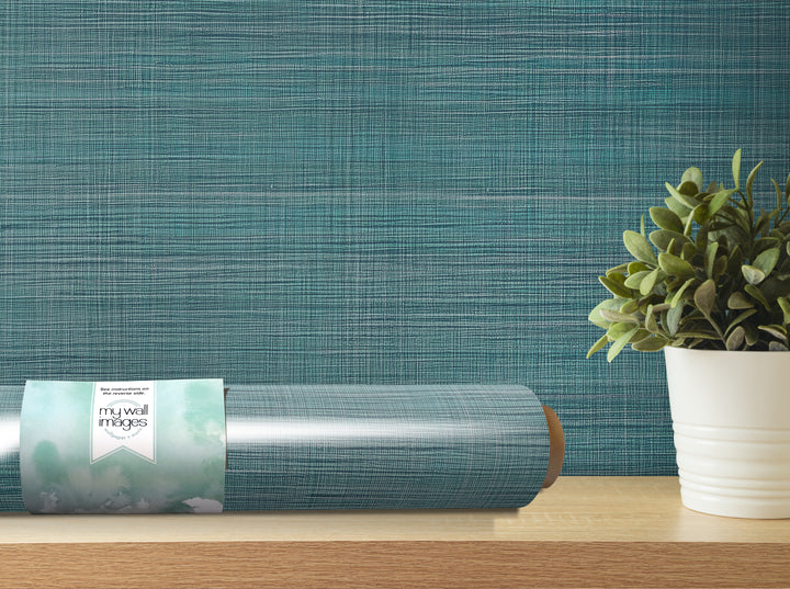 a roll of wallpaper with a teal blue pattern, placed on a wooden shelf next to a potted plant.