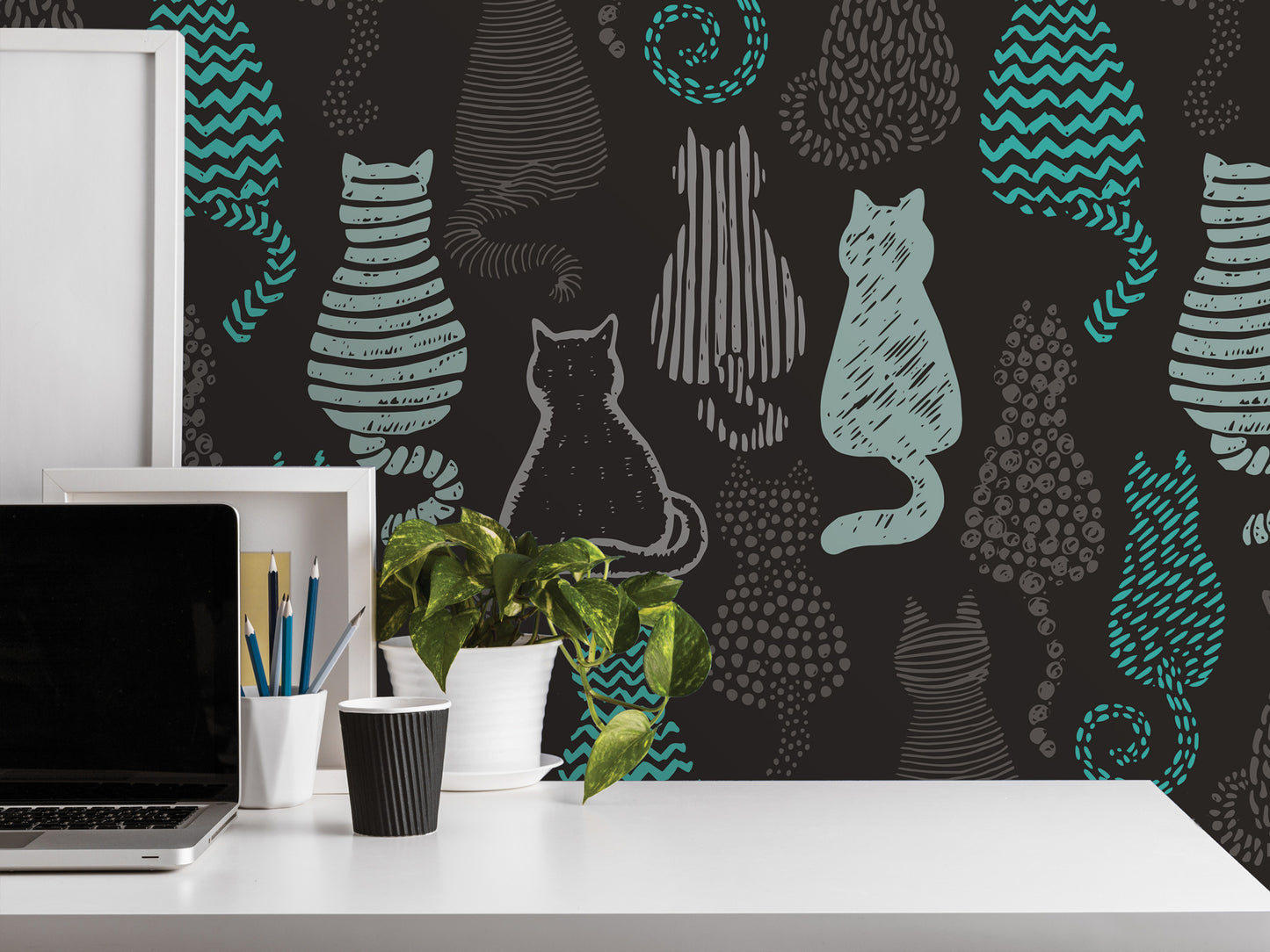 a workspace with a laptop, a plant, and various office supplies on a white desk. The wall behind the desk has a repeating pattern of cat silhouettes in shades of gray and blue, creating a whimsical and playful atmosphere.