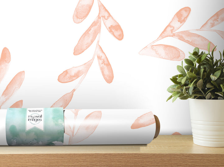 a roll of wallpaper with a watercolor leaf pattern, placed on a wooden shelf next to a potted plant.