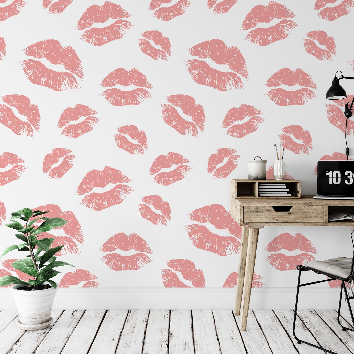 a wallpapered wall with a repeating pattern of pink lips against a white background. There is a wooden desk with a laptop and a plant on it, and a chair is positioned next to the desk.