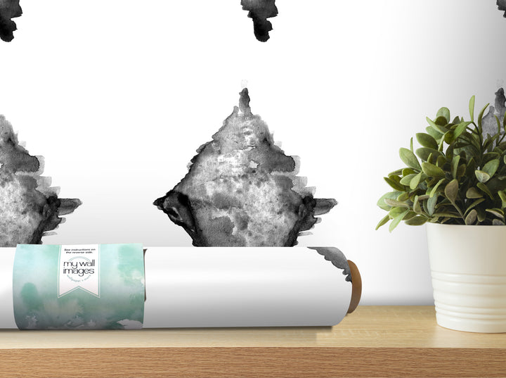 a white wall with a black and white abstract watercolor painting hanging on it, along with a potted plant and a roll of wallpaper on a shelf.