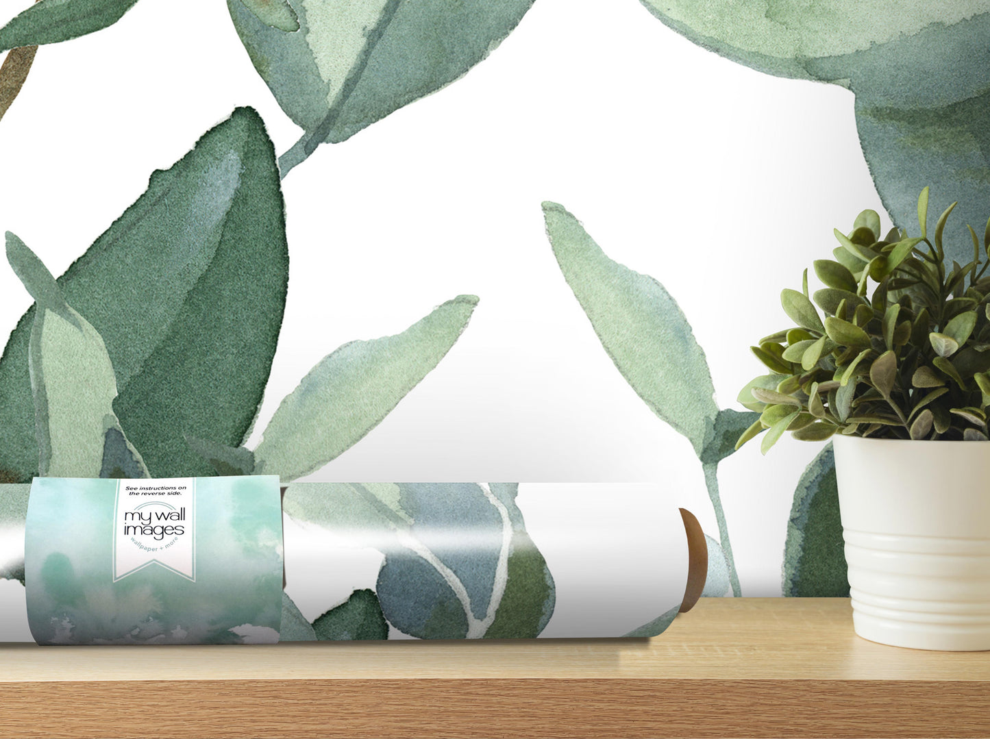 a roll of wallpaper with a watercolor-style leaf pattern, placed on a wooden shelf next to a potted plant.