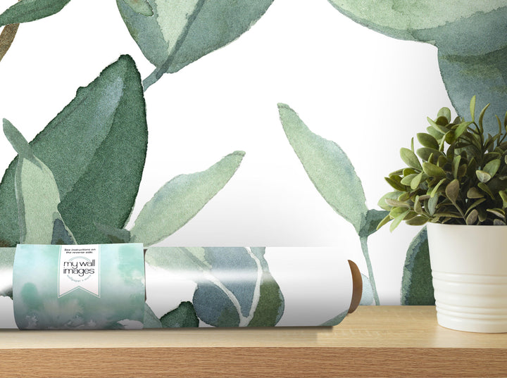 a roll of wallpaper with a watercolor-style leaf pattern, placed on a wooden shelf next to a potted plant.