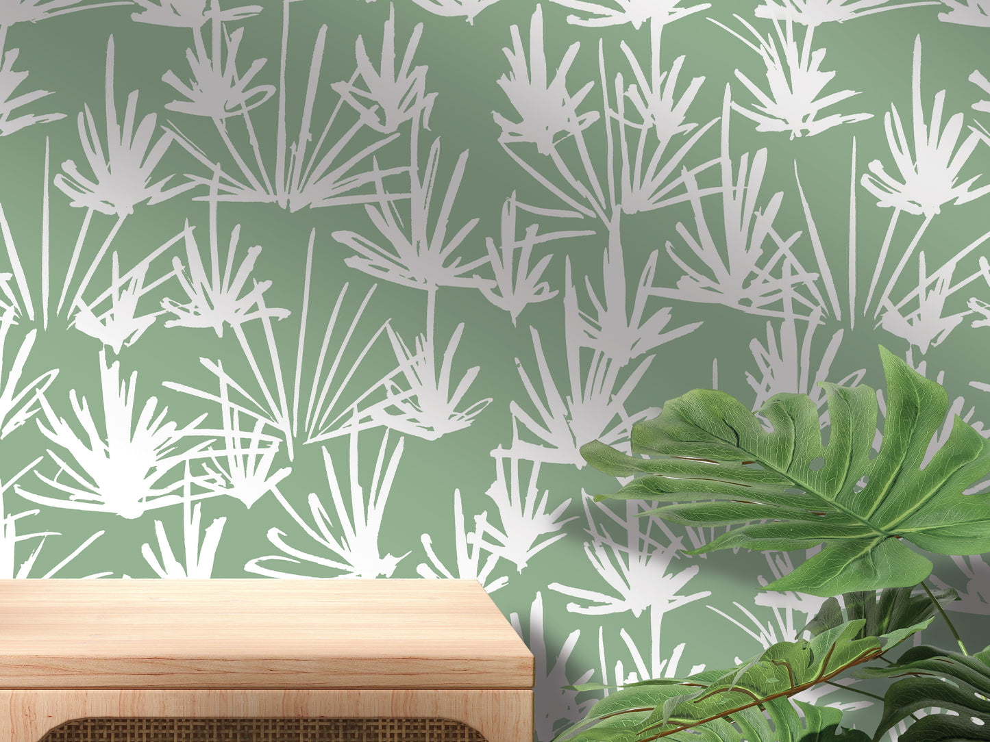 a wall with a repeating pattern of white and green leaves, creating a tropical or nature-inspired design. In the foreground, there is a wooden table or shelf, and a large green leaf is visible on the right side of the image.