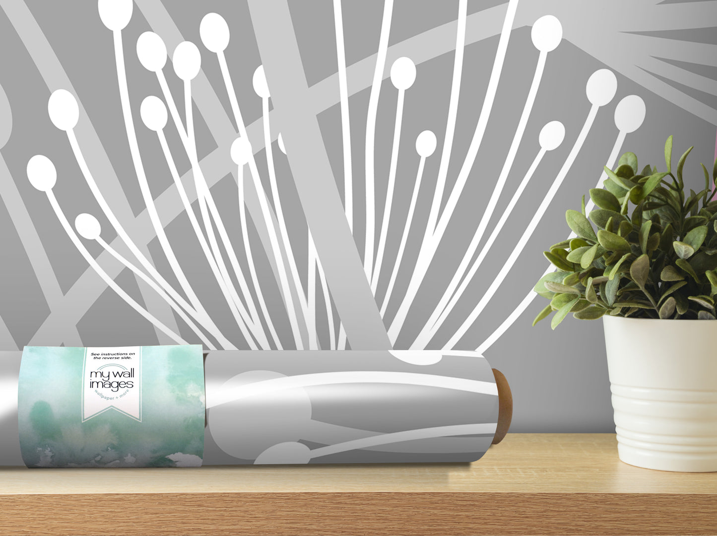 a grey and white abstract design on a wall, with a potted plant and a roll of wallpaper or decal on a wooden surface in the foreground.