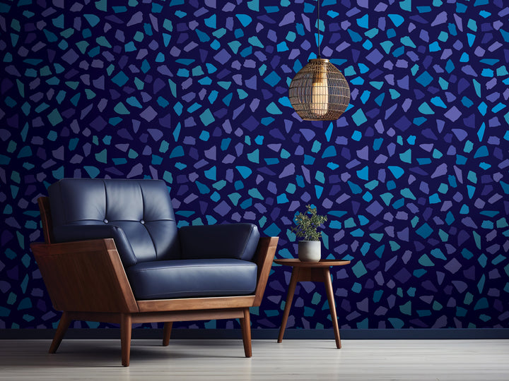 a modern living room with a blue leather armchair, a wooden side table, and a hanging light fixture. The wall behind the furniture has a mosaic pattern in shades of blue and purple.