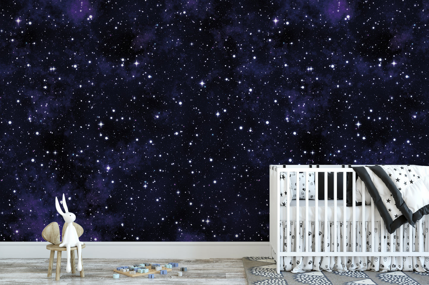 a nursery room with a white crib and a white stuffed rabbit sitting on a wooden chair. The room has a starry night sky mural on the wall, creating a serene and calming atmosphere.
