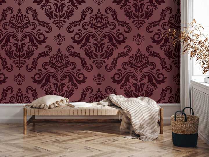 a room with a large burgundy wallpapered wall, a wooden bench with a blanket draped over it, and a woven basket on the floor.