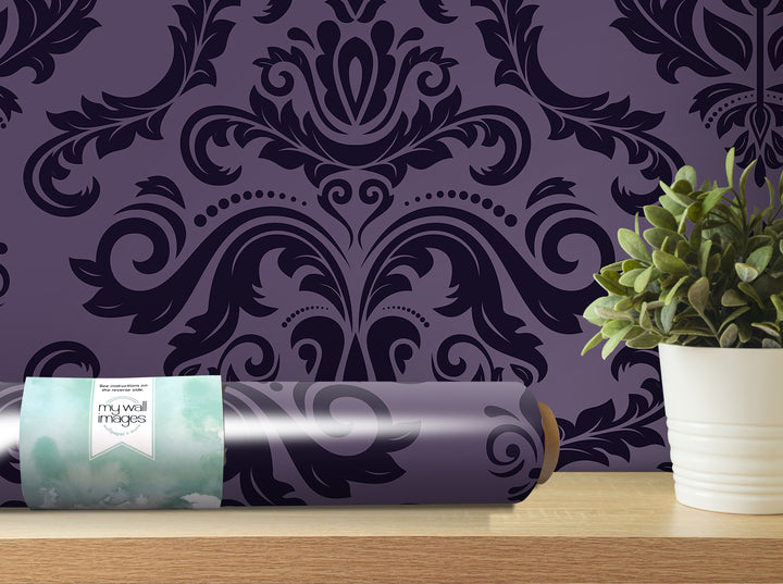 a purple wallpaper with a black and white damask pattern, a potted plant, and a roll of wallpaper on a shelf.