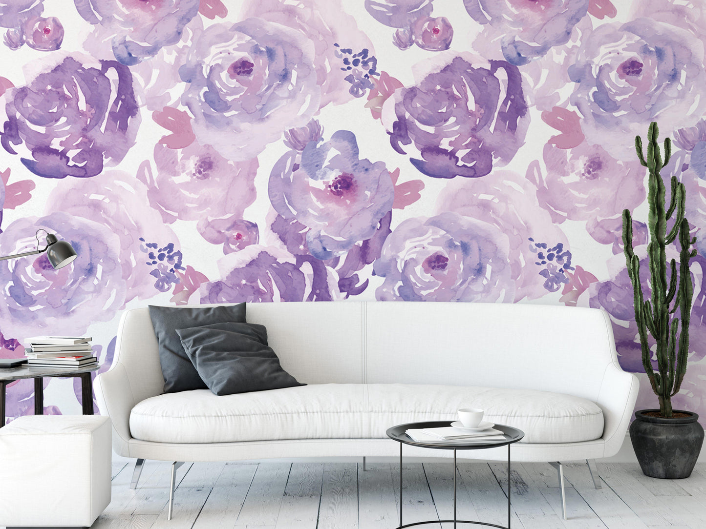 a living room with a white sofa and a coffee table in front of it. The wall behind the sofa is decorated with a large floral wallpaper in shades of purple and pink. There are also some books and a potted plant in the room, adding to the cozy and inviting atmosphere.