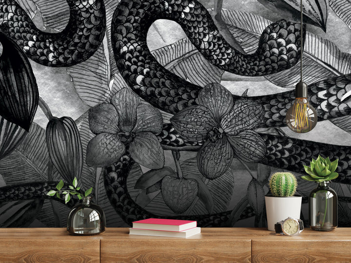 a wooden shelf with various decorative items, including a cactus plant, a book, a clock, and a vase. The shelf is set against a wall with a striking black and white mural depicting a snake and floral elements.
