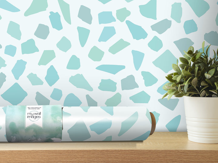 a roll of wallpaper with a pattern of blue and green shapes, placed on a wooden shelf next to a potted plant.