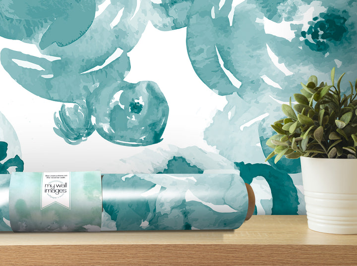 a roll of wallpaper with a watercolor-style floral pattern, placed on a wooden shelf next to a potted plant.