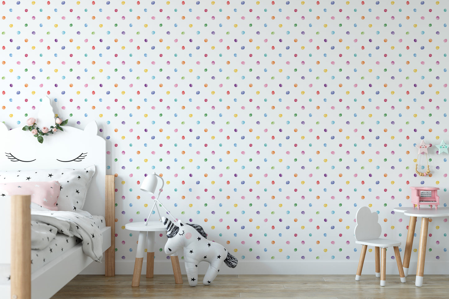 A child's bedroom with a white bed, a small table, and a chair. The walls are covered in a polka dot pattern, and there is a stuffed animal on the floor.