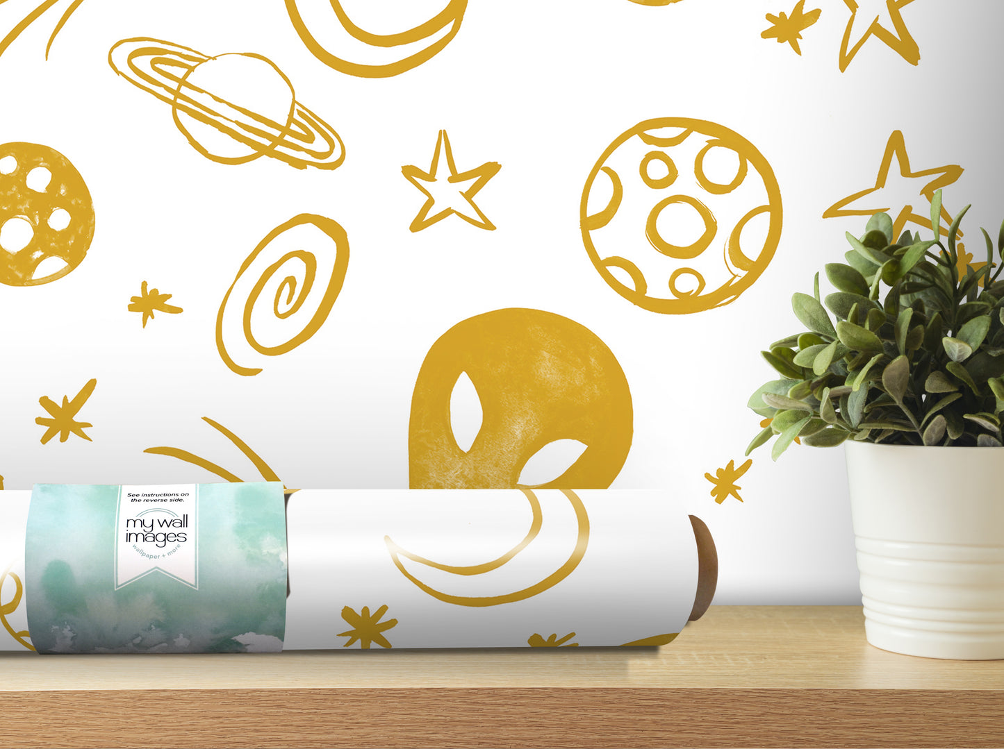 a wall with a white and gold pattern of planets, stars, and other celestial objects, along with a potted plant and a roll of wallpaper on a shelf.