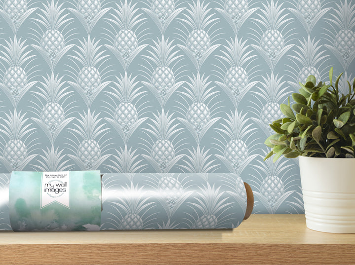 a roll of wallpaper with a repeating pineapple pattern, placed on a wooden shelf next to a potted plant.