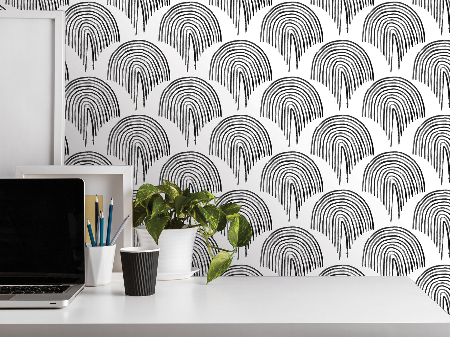 a white desk with various items on it, including a laptop, a plant, and some office supplies. The wall behind the desk has a repeating pattern of black and white arches, creating a visually striking backdrop.