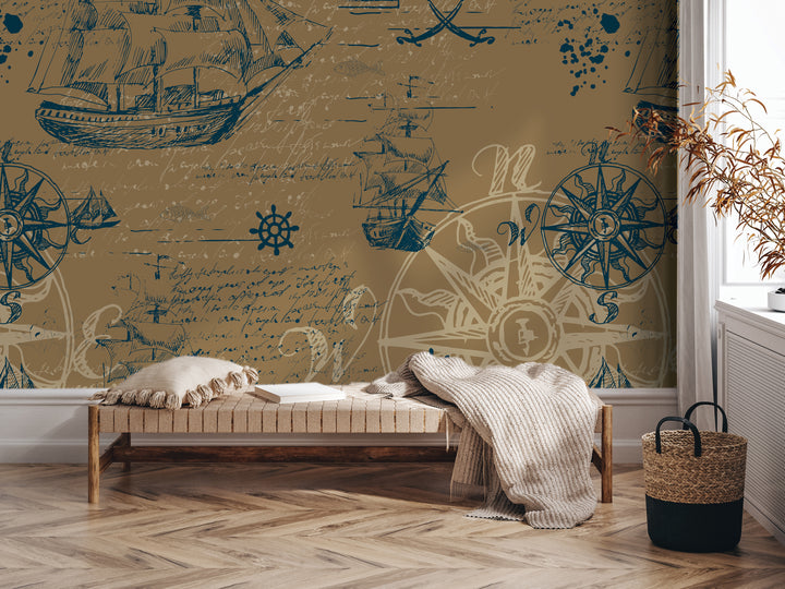 a room with a large wall mural depicting nautical scenes, including ships, a compass, and other maritime elements. In the foreground, there is a bench with a blanket draped over it, and a woven basket is placed nearby. The room has a wooden floor and a window, creating a cozy and inviting atmosphere.