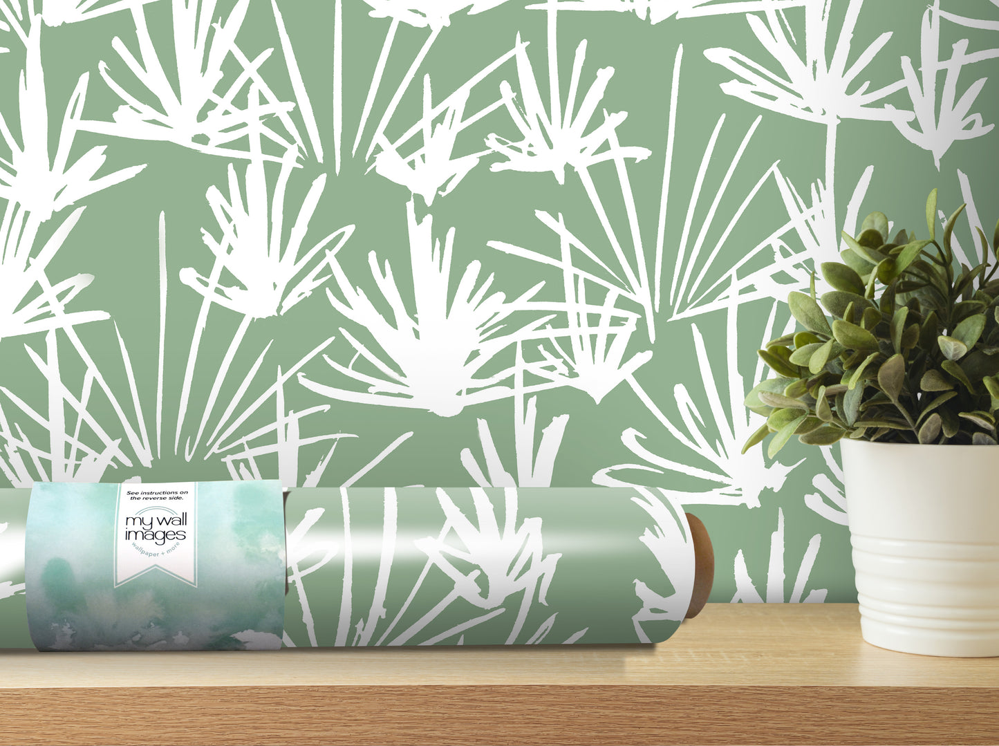 a roll of wallpaper with a white and green leafy pattern, placed on a wooden shelf next to a potted plant.