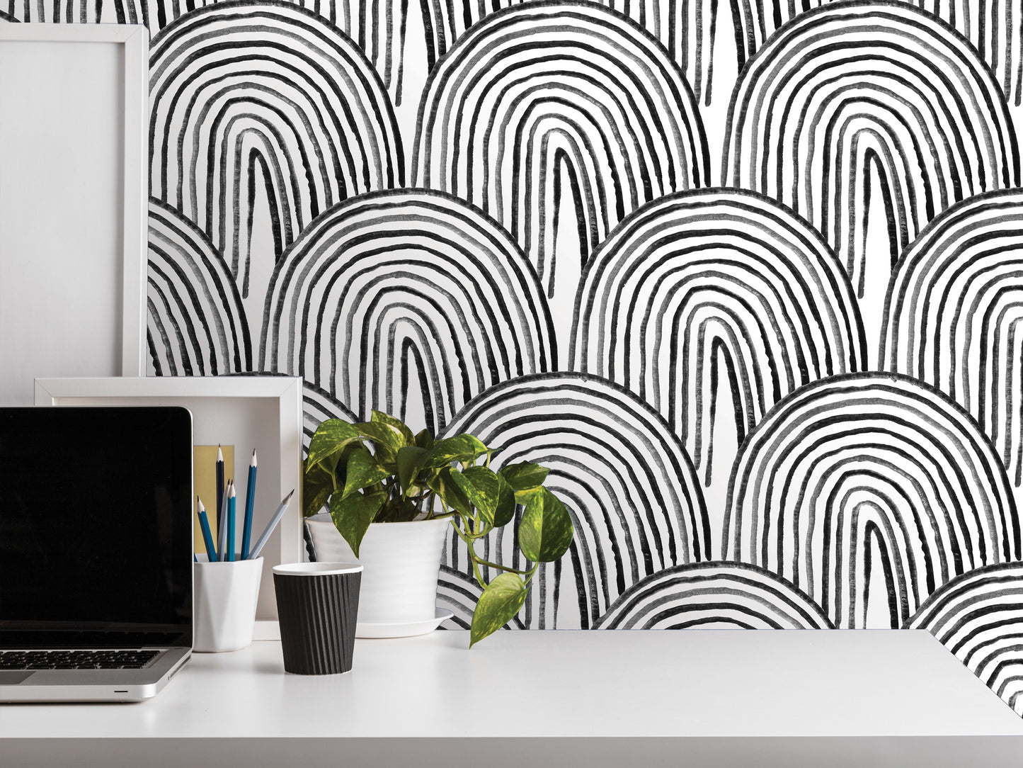 a workspace with a laptop, a plant, and various office supplies on a white desk. The wall behind the desk has a striking black and white abstract pattern, creating a visually appealing backdrop for the workspace.