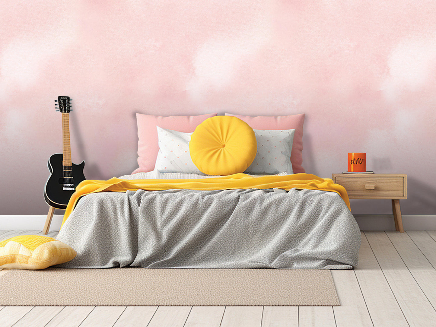 a bedroom with a bed, a guitar, and a nightstand. The bed has a gray comforter and a yellow throw pillow. The guitar is leaning against the wall, and the nightstand has a book and a mug on it. The walls are painted pink, and the floor is made of wood.