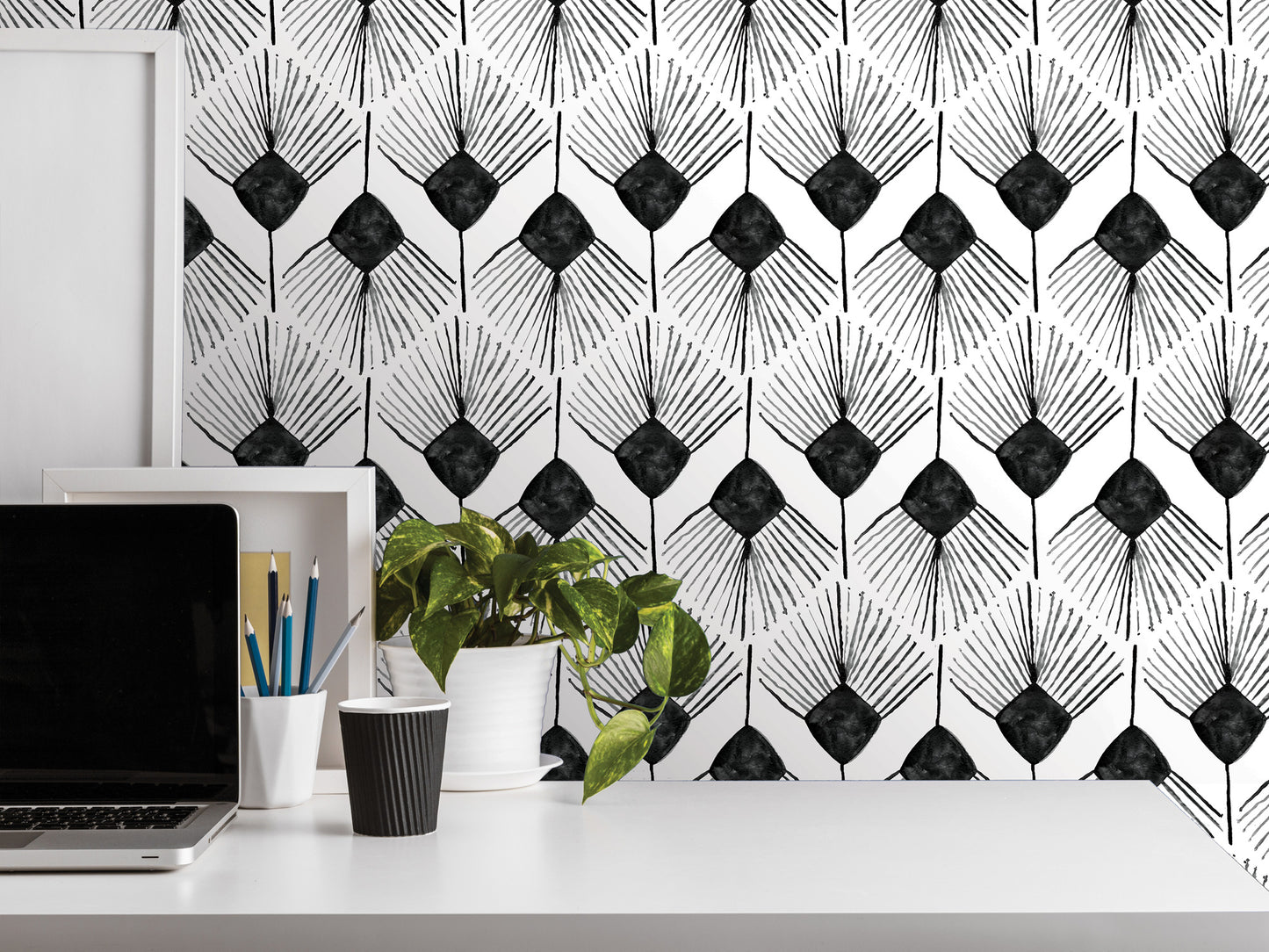 a white desk with various items on it, including a laptop, a plant, a cup, and a framed picture. The background has a black and white geometric pattern.