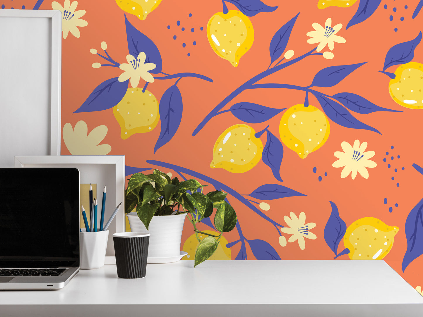 a workspace with a laptop, a plant, and various office supplies on a white desk. The background wall is decorated with a vibrant pattern of yellow lemons and blue leaves, creating a lively and cheerful atmosphere.