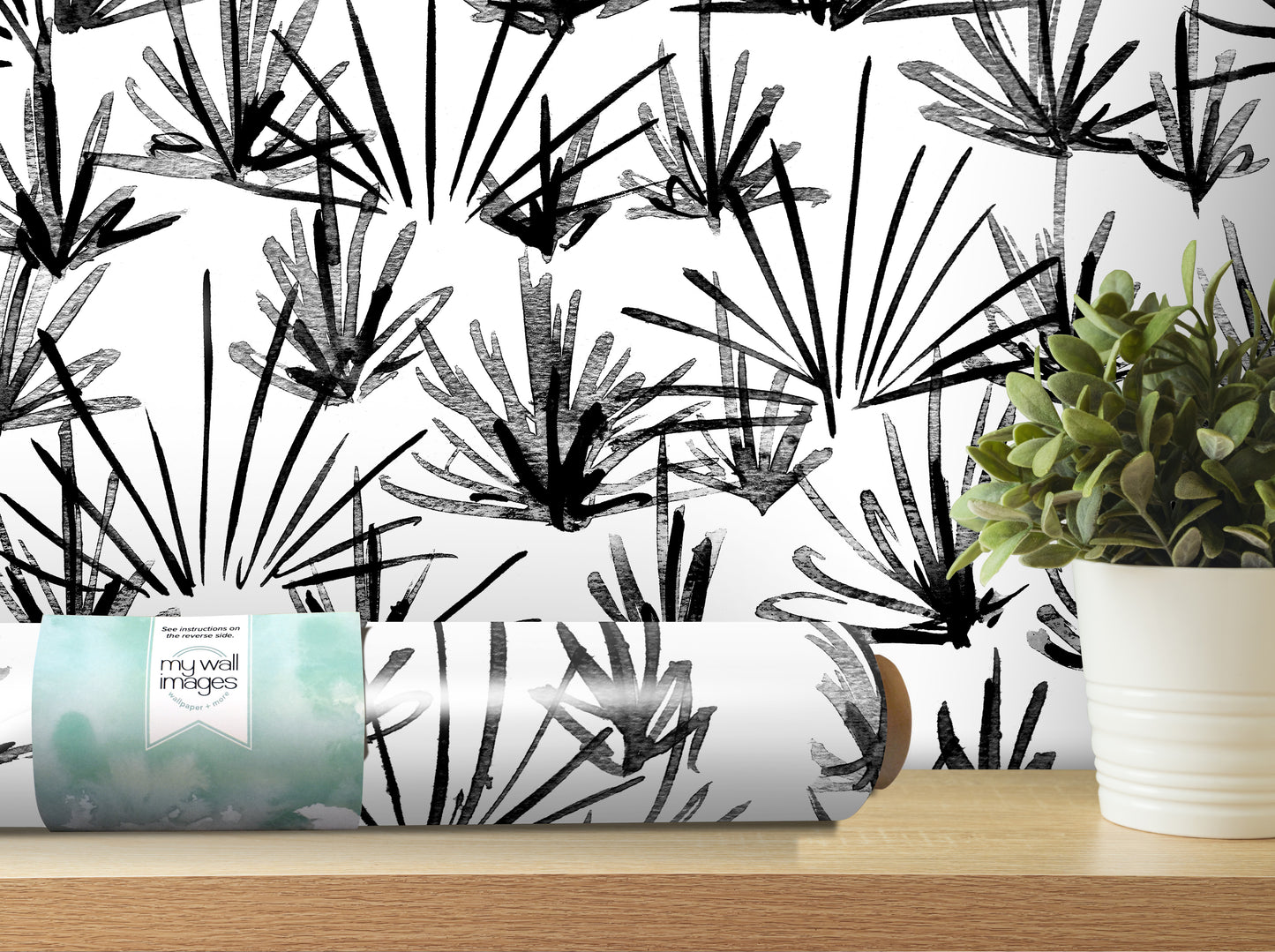 a black and white abstract pattern on a wall, with a potted plant and a roll of wallpaper or paper with a similar design on a shelf in the foreground.