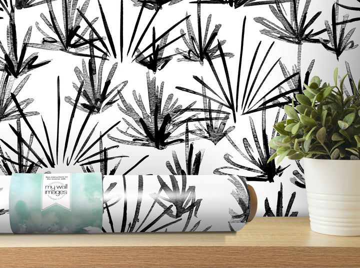 a black and white abstract pattern on a wall, with a potted plant and a roll of wallpaper or paper with a similar design on a shelf in the foreground.
