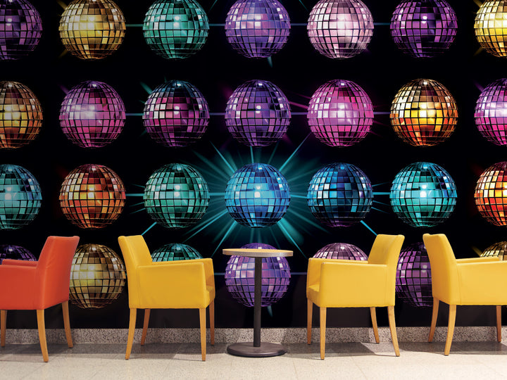 a vibrant and colorful disco ball display, with numerous disco balls of various sizes and colors arranged in a grid-like pattern against a dark background. In the foreground, there are four yellow chairs arranged around a small round table, creating a cozy and inviting atmosphere.