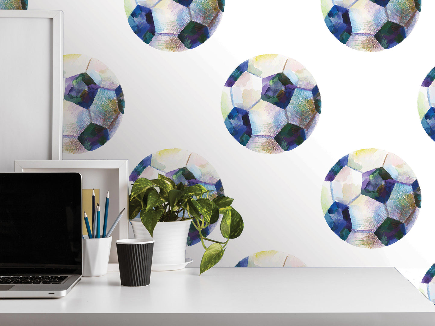 a white desk with a laptop, a plant, and a cup of coffee. The desk is set against a wall with a repeating pattern of colorful soccer balls.