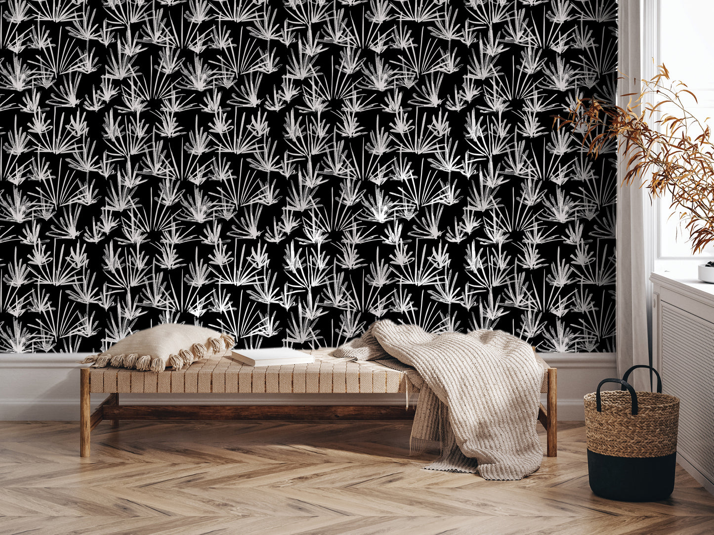 a black and white patterned wallpaper with a repeating design of white flowers or leaves, creating a striking visual effect. In the foreground, there is a wooden bench with a beige blanket draped over it, and a woven basket next to it. The arrangement of these objects suggests a cozy and inviting atmosphere.