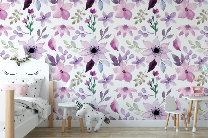 a child's bedroom with a white bed, a small table, and a stuffed animal. The walls are decorated with a floral pattern in shades of purple and pink, creating a cheerful and playful atmosphere.