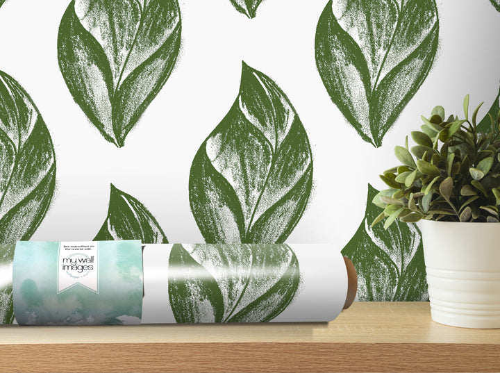 a roll of wallpaper with a repeating pattern of green leaf designs, placed on a wooden shelf next to a potted plant.