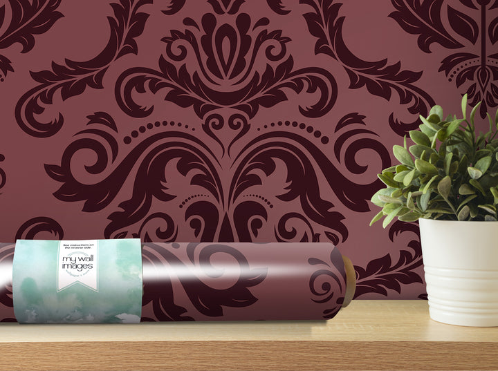 a decorative purple wallpaper with an ornate floral pattern, a potted plant, and a roll of wallpaper on a shelf.
