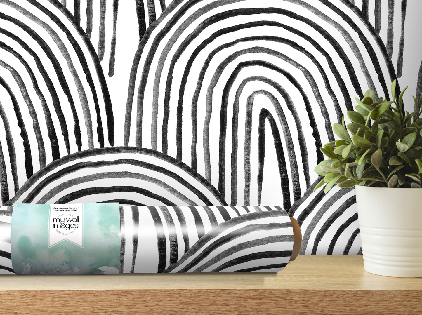 a black and white abstract pattern on a wall, with a potted plant and a roll of wallpaper on a shelf in the foreground.