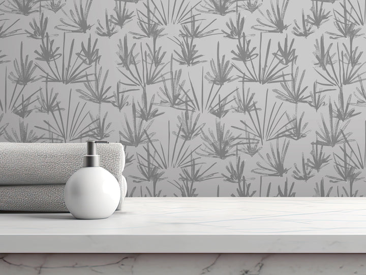 a white soap dispenser on a white countertop, with a gray towel and a white bottle of lotion placed next to it. The background is a gray wall with a repeating pattern of stylized plants or flowers.