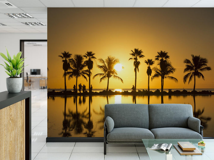 a large wall mural depicting a serene beach scene with palm trees silhouetted against a sunset. The mural is the focal point of the room, with a comfortable gray sofa and a glass coffee table in the foreground.