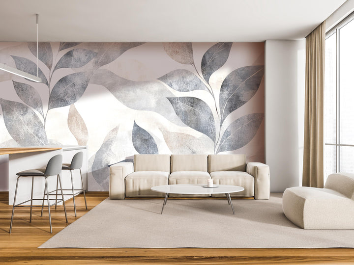 a modern living room with a large wall mural featuring abstract leaf designs in shades of gray and beige. The room is furnished with a white sofa, a round coffee table, and a barstool set. The overall design and color scheme create a serene and contemporary atmosphere.