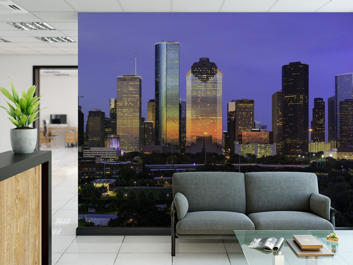 a modern office space with a large wall mural depicting a nighttime cityscape with tall skyscrapers illuminated by colorful lights. In the foreground, there is a gray sofa and a glass coffee table.