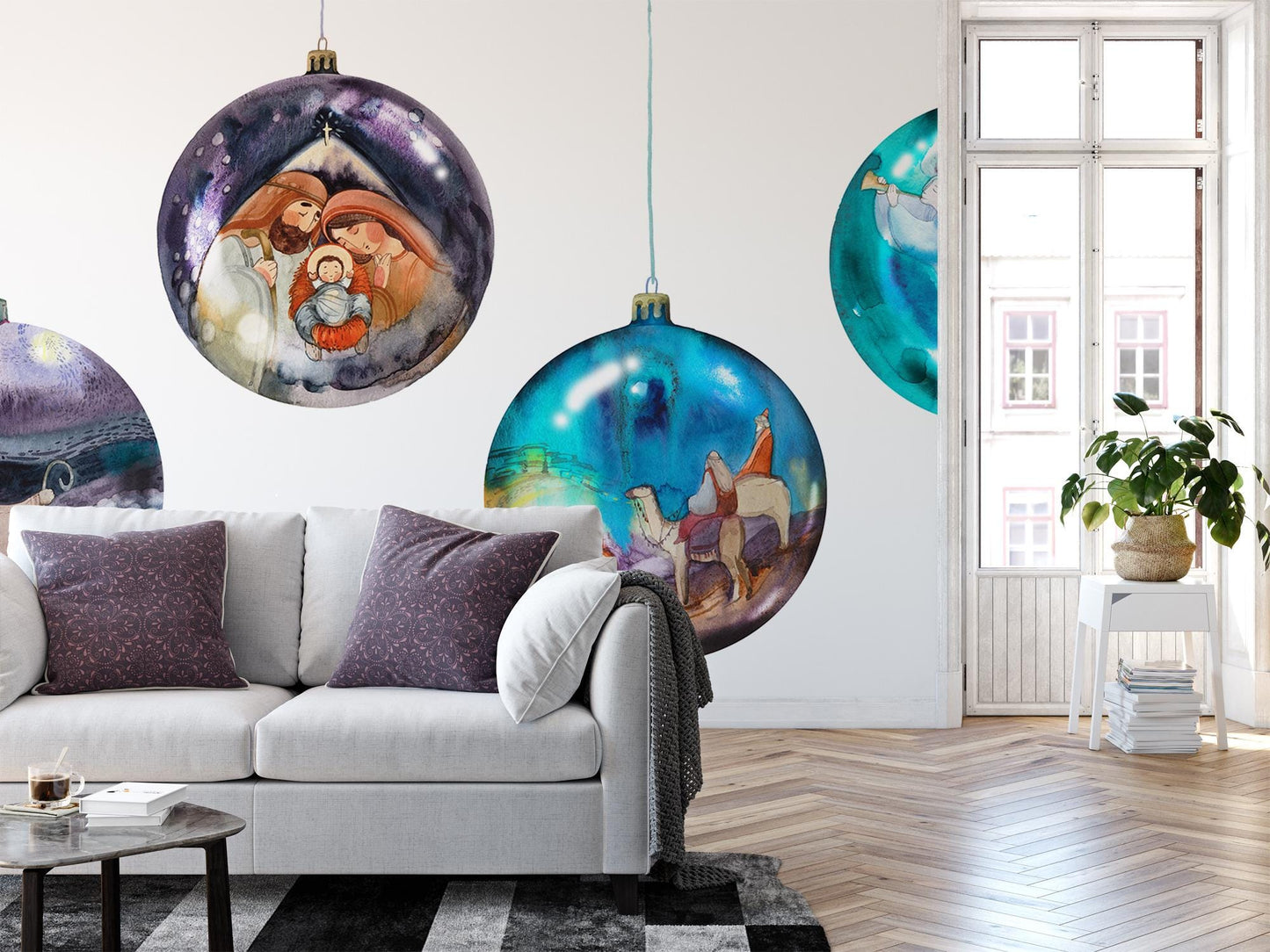 a living room with a white couch, a coffee table, and a large window. Above the couch, there are three large, colorful Christmas ornaments hanging on the wall, depicting scenes from the nativity.