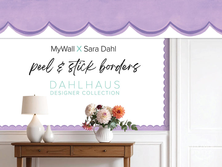 a wooden table with a vase of flowers, a lamp, and a purple border on the wall behind it.