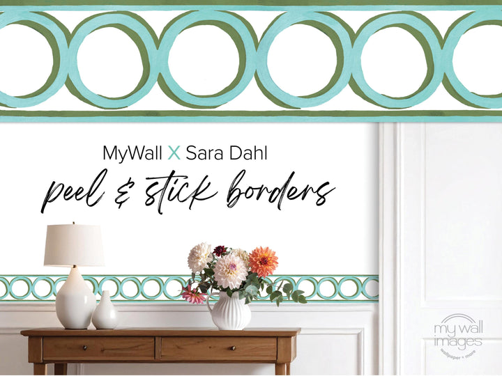 a wooden table with a vase of flowers, a lamp, and a geometric patterned border along the wall.
