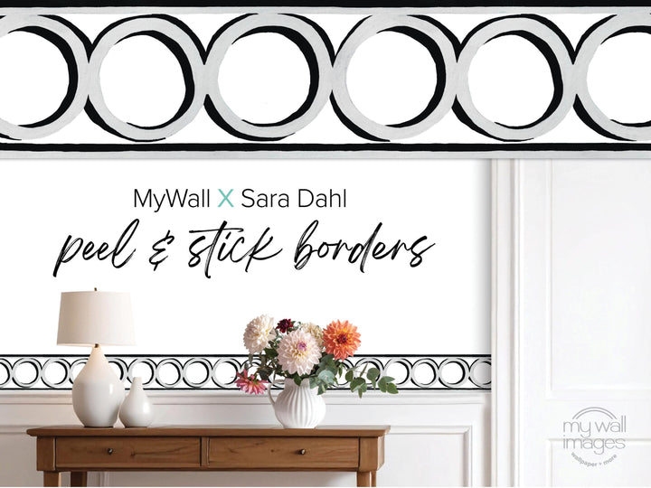 a wooden table with a vase of flowers, a lamp, and a black and white geometric border design on the wall behind it.