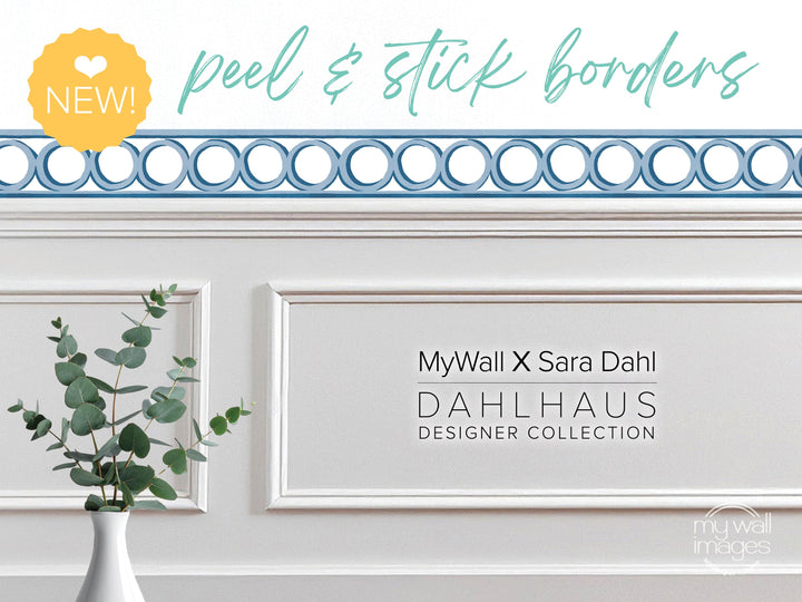 a white wall with a decorative border, a vase of green leaves, and text that reads &quot;MyWall X Sara Dahl Dahlhaus Designer Collection&quot;.