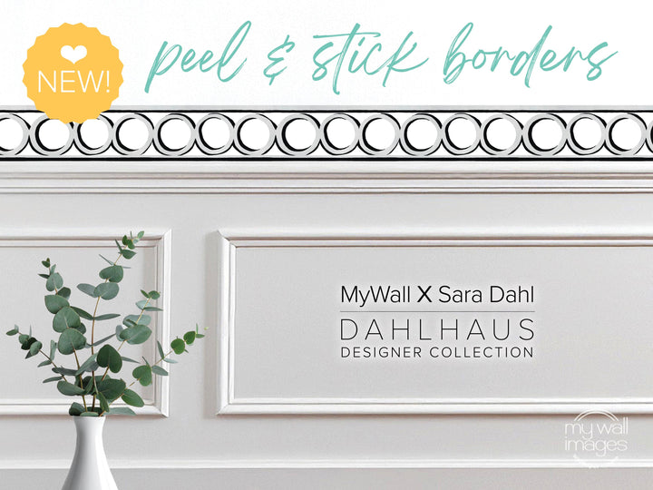 a white wall with a decorative border, a vase of greenery, and text that reads &quot;MyWall X Sara Dahl Dahlhaus Designer Collection&quot;.